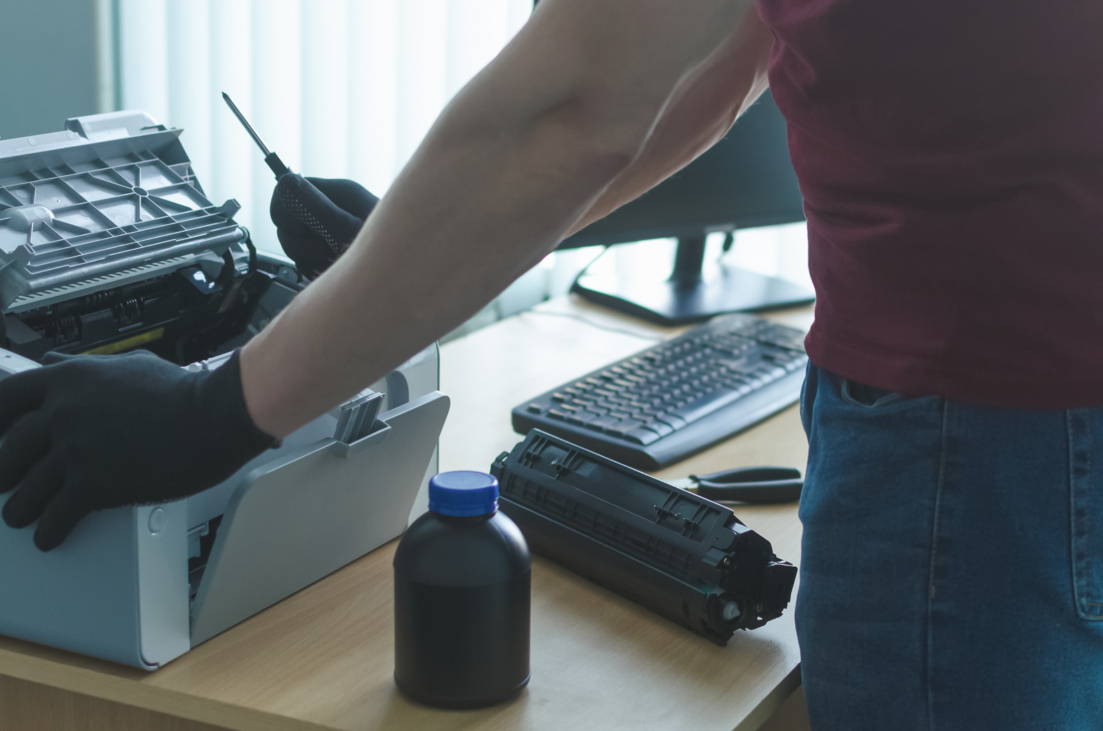 Ein Mann wechselt den Toner eines Laserdruckers mit einem Schraubendreher in der Hand.
